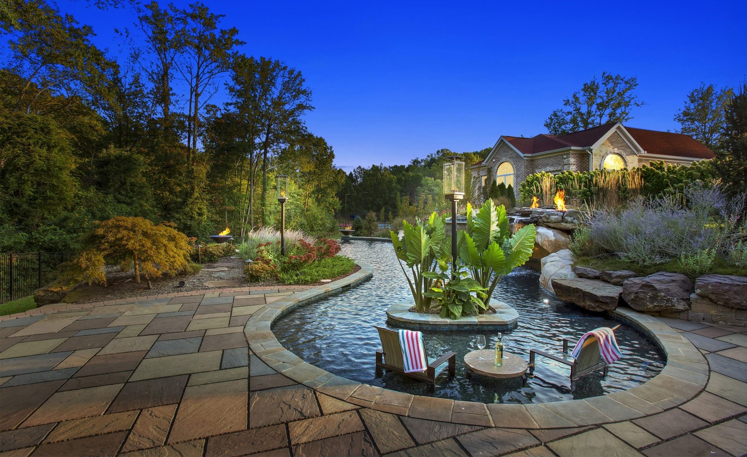 Luxury backyard with custom stone patio, pool, and integrated landscape lighting at dusk