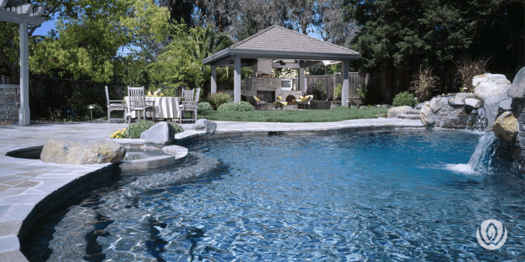 Backyard pool with stone waterfall, rock formations, and wooden pavilion seating area