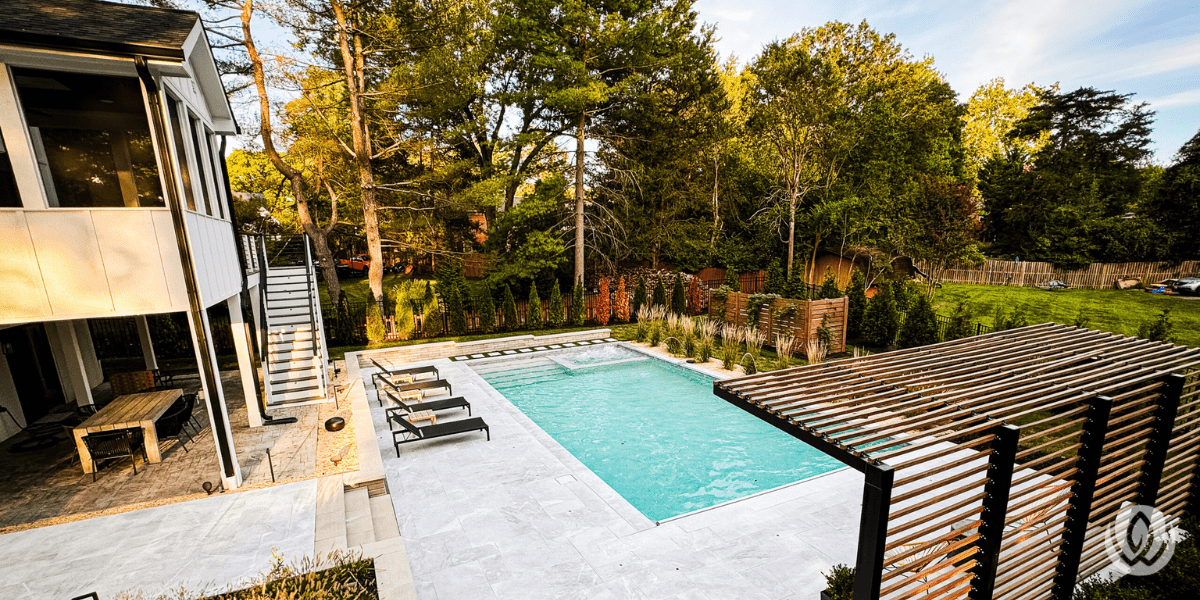 Custom backyard pool with stone patio, pergola, and landscaped trees