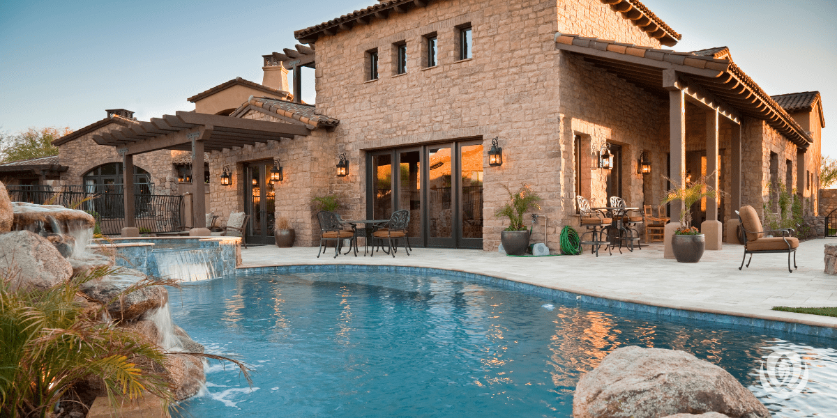 Luxury backyard pool with stone patio and covered outdoor living area at dusk