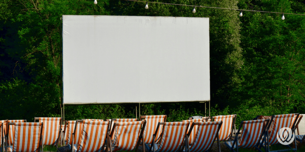 Fixed frame outdoor movie screen mounted in a backyard with striped lounge seating